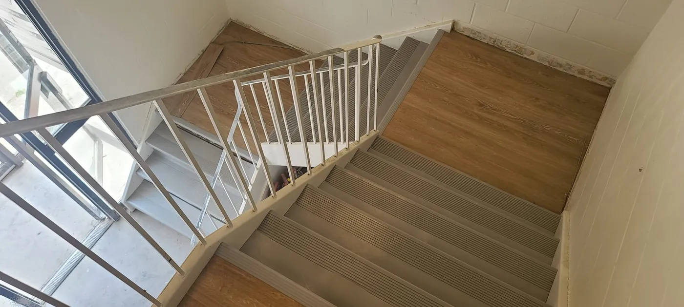 Commercial stairwell with ribbed rubber stair treads on every step and wood-look LVT on the landings, installed by Geometrix
